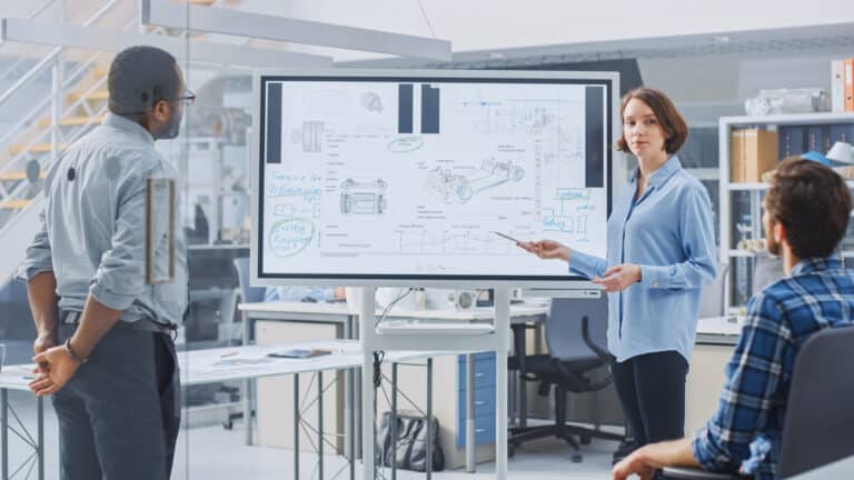 Woman giving work presentation to two colleagues using interactive whiteboard